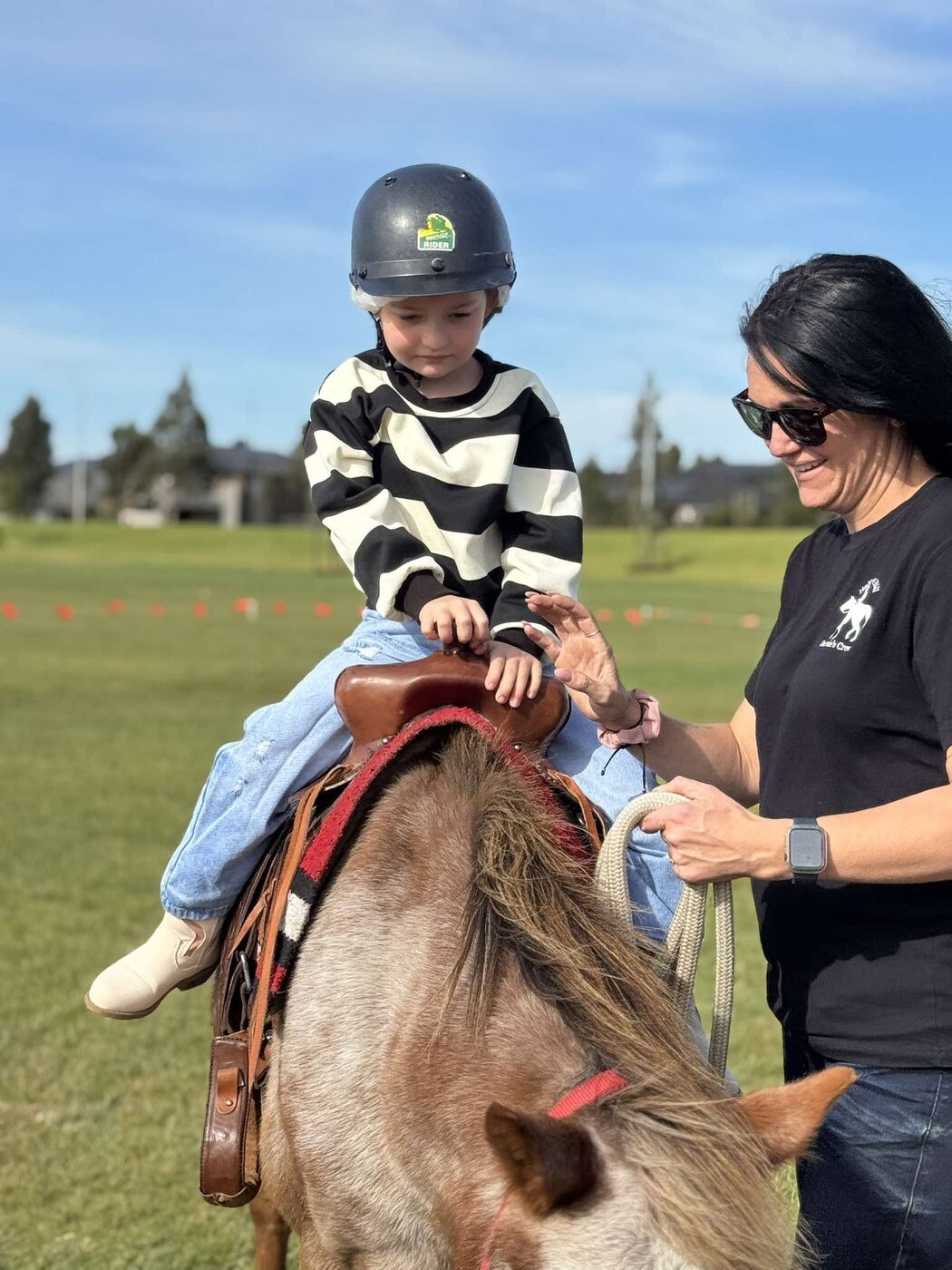 A helmeted young rider being assisted by an experienced Little Riders handler
